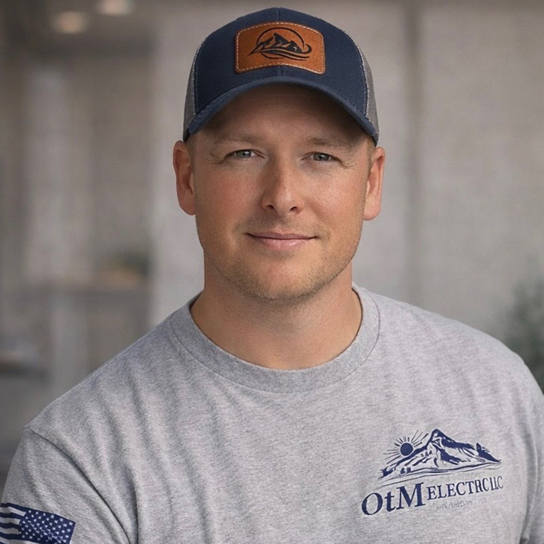 Man in OtM Electric LLC shirt and cap, smiling indoors.